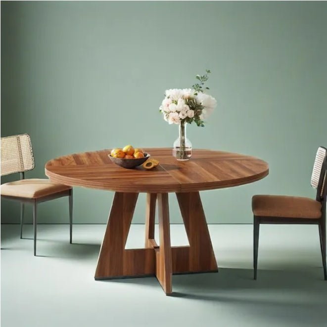 Wooden dining table with a bowl of fruit and a vase of flowers, set against a green wall.