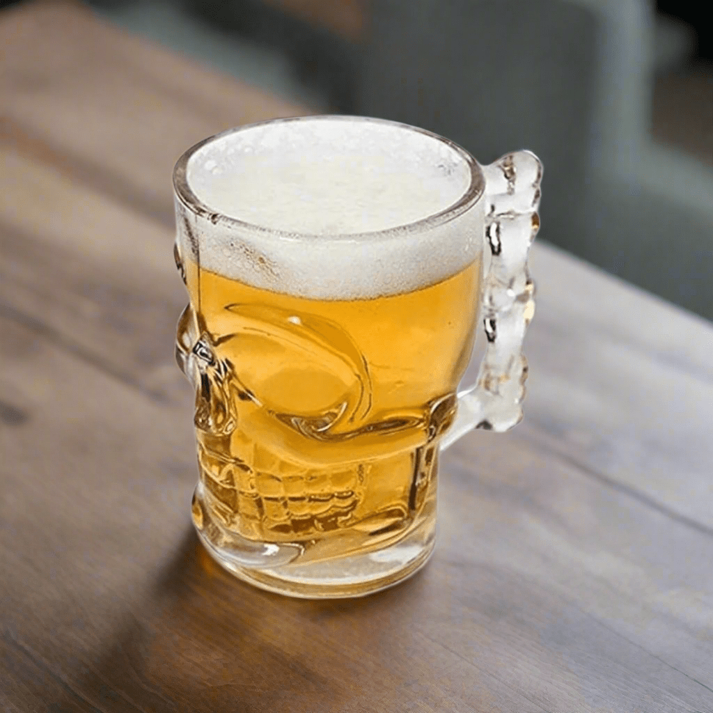 Clear glass skull-handled beer mug filled with frothy beer on a wooden table.