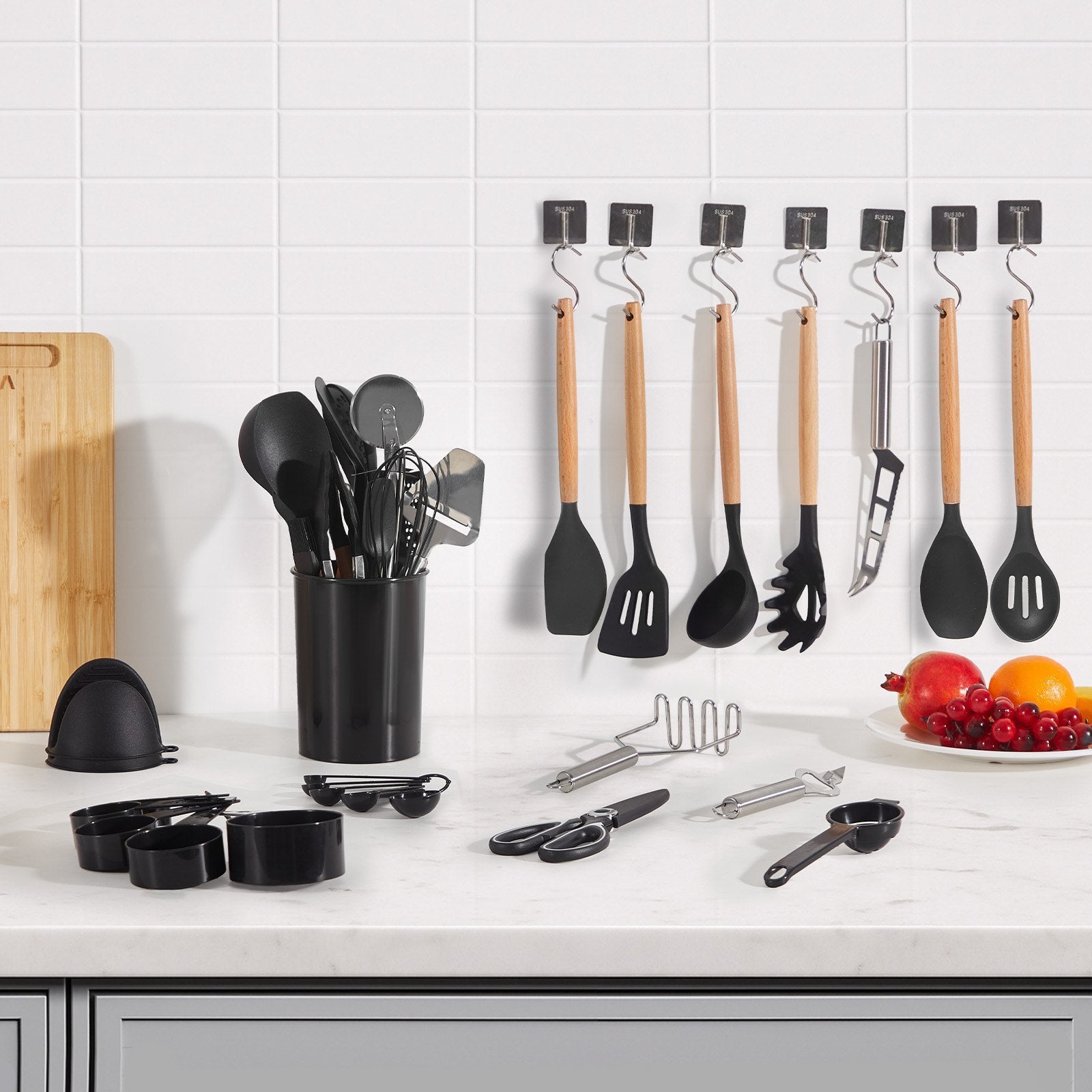 Kitchen utensils including spatulas, ladles, and measuring cups on a countertop with a tiled wall background.