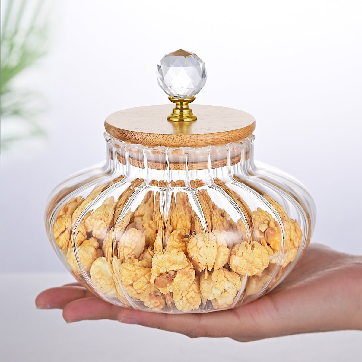Clear glass jar with wooden lid filled with snacks, held by a hand on a light background