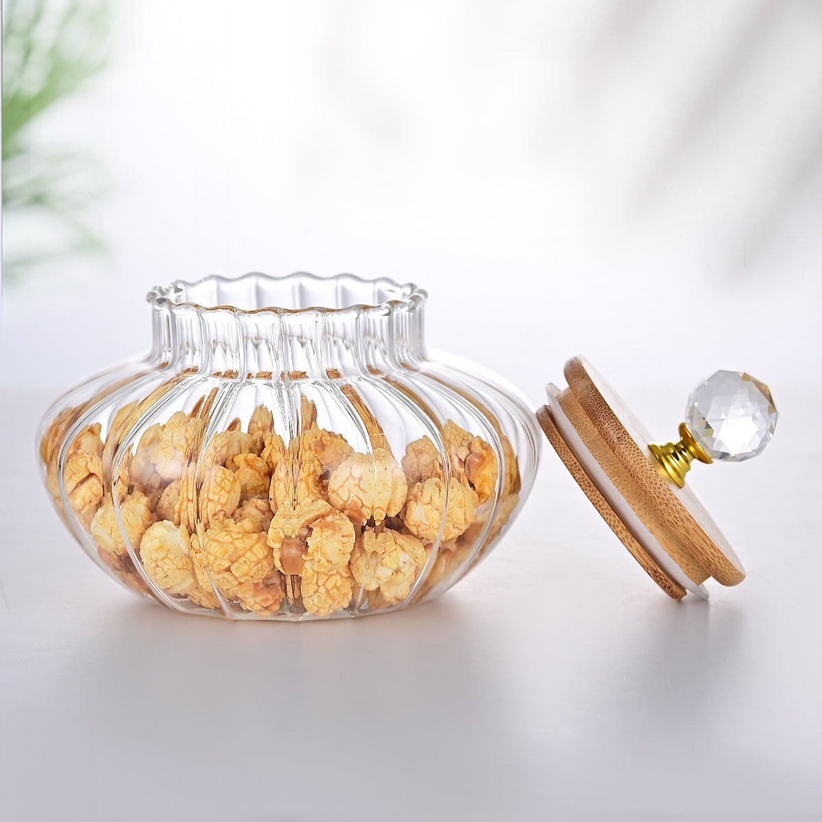 Clear glass jar with wooden lid containing dried flowers on a light background