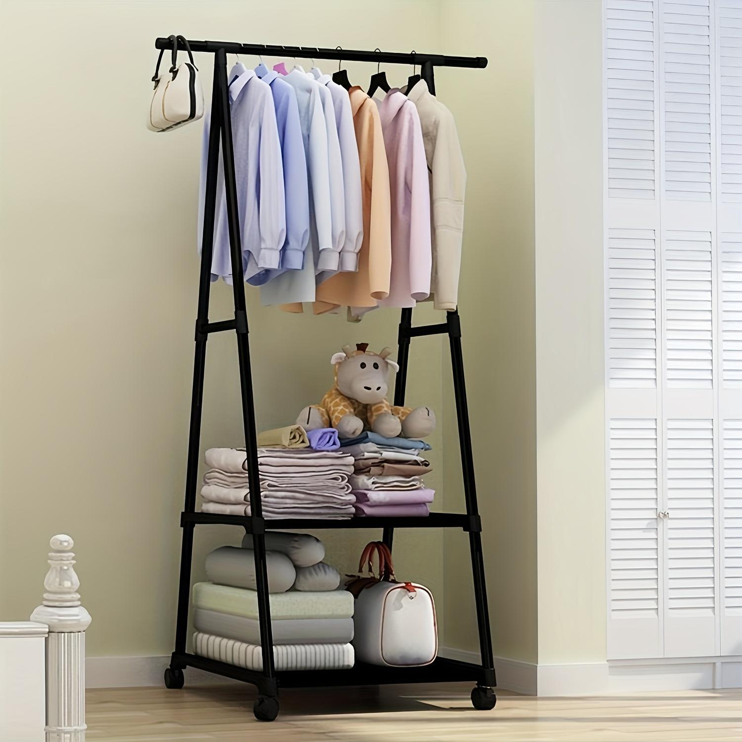 Black clothing rack with clothes, folded blankets, and a teddy bear against a beige wall.