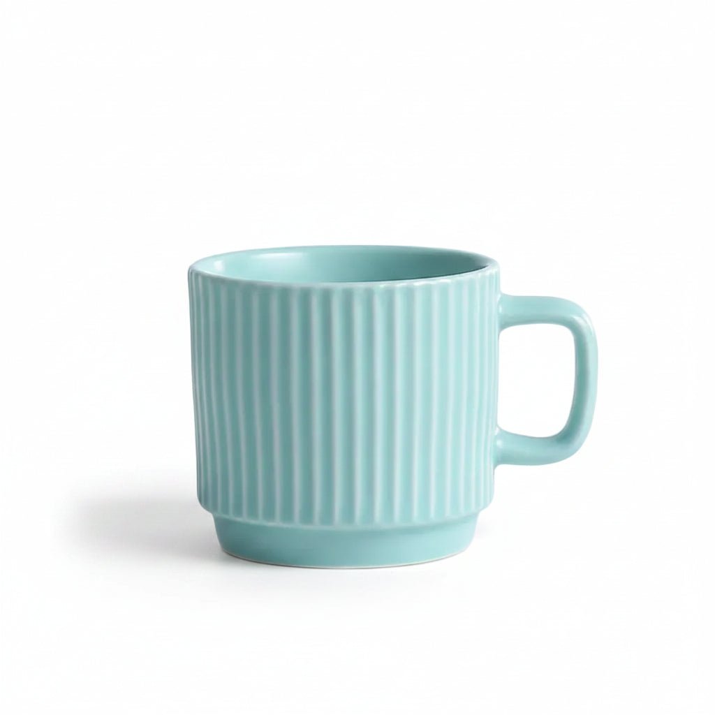 A light mint green ceramic mug with vertical fluted ridges and a matching handle, sitting on a white textured lace cloth with a decorative cream-colored candle partially visible on the left.