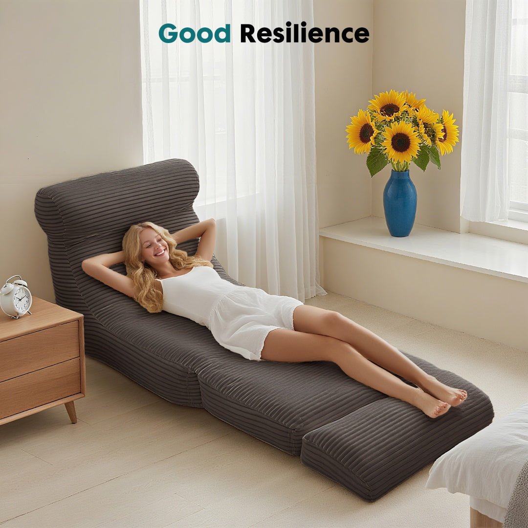 Woman relaxing on a brown lounge chair in a bright room with a vase of sunflowers.