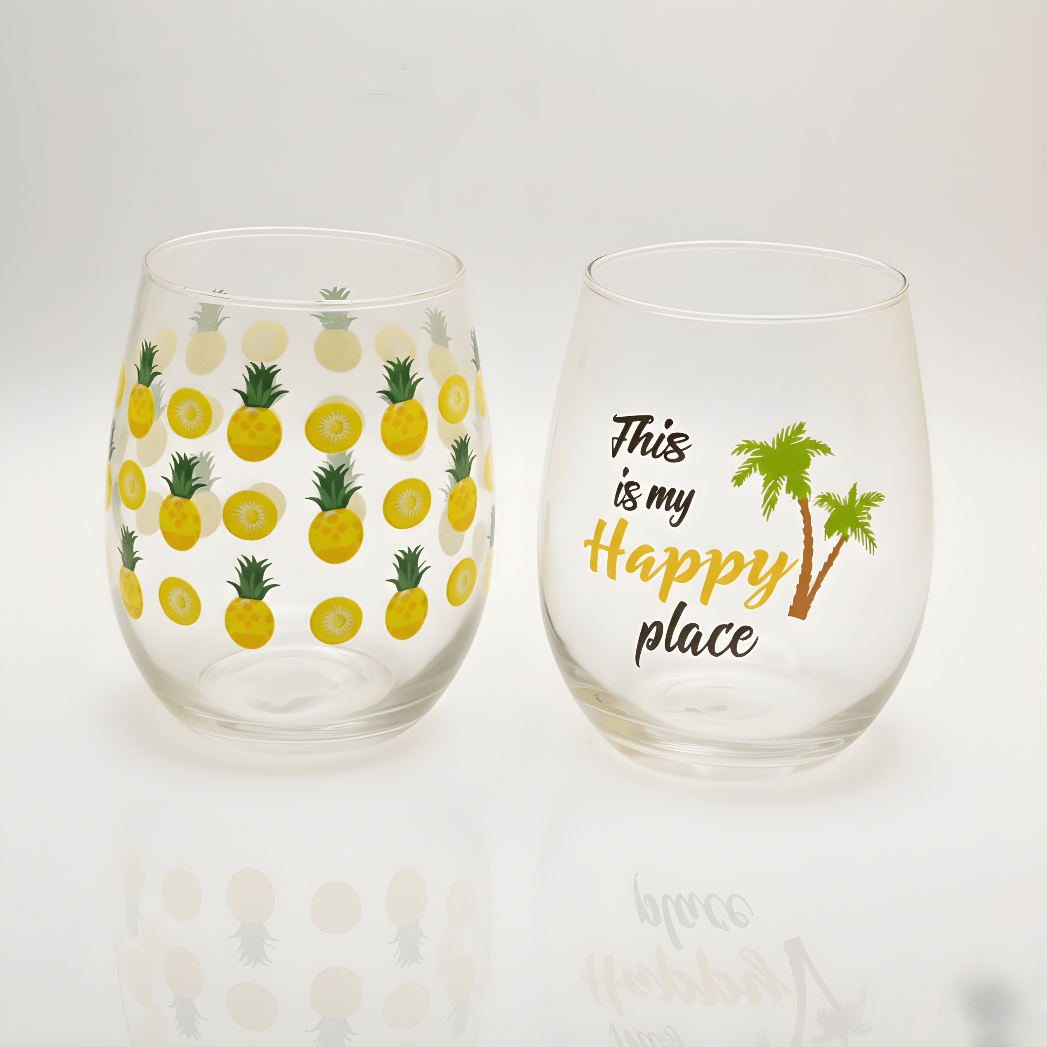 Two stemless wine glasses with pineapple pattern and 'Happy Place' text on a white background
