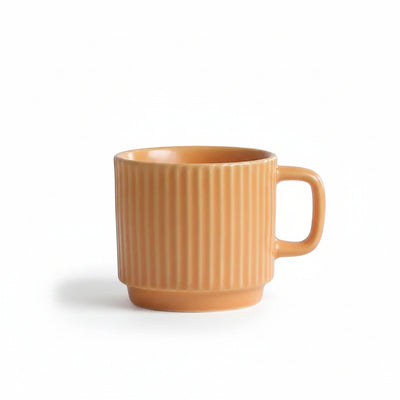 An orange ceramic mug with a ribbed vertical texture and a C-shaped handle, sitting on a white textured tablecloth with a soft gray background.