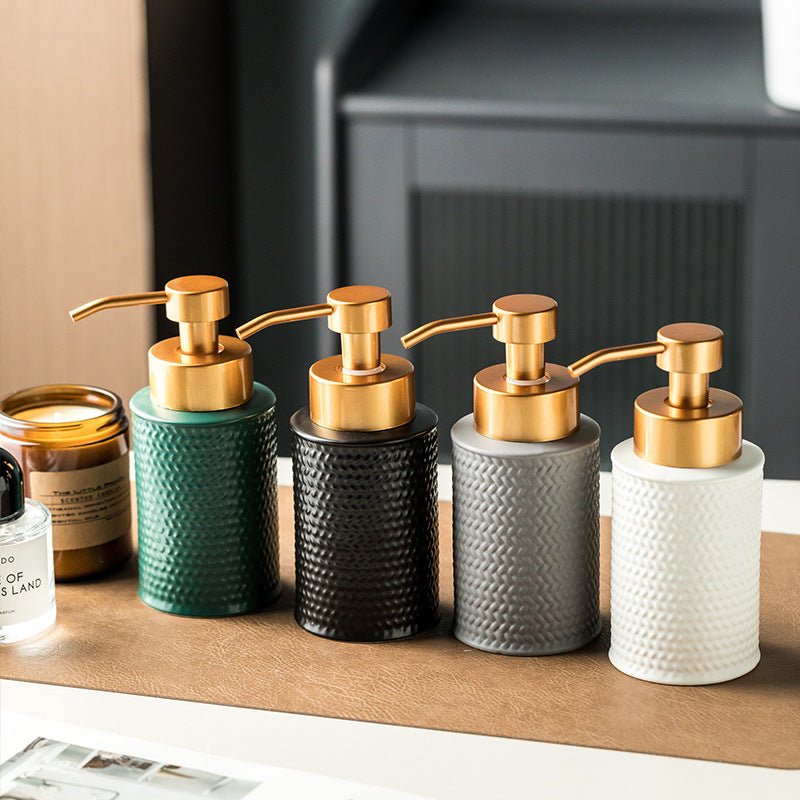 Four soap dispensers with gold pumps on a wooden surface.