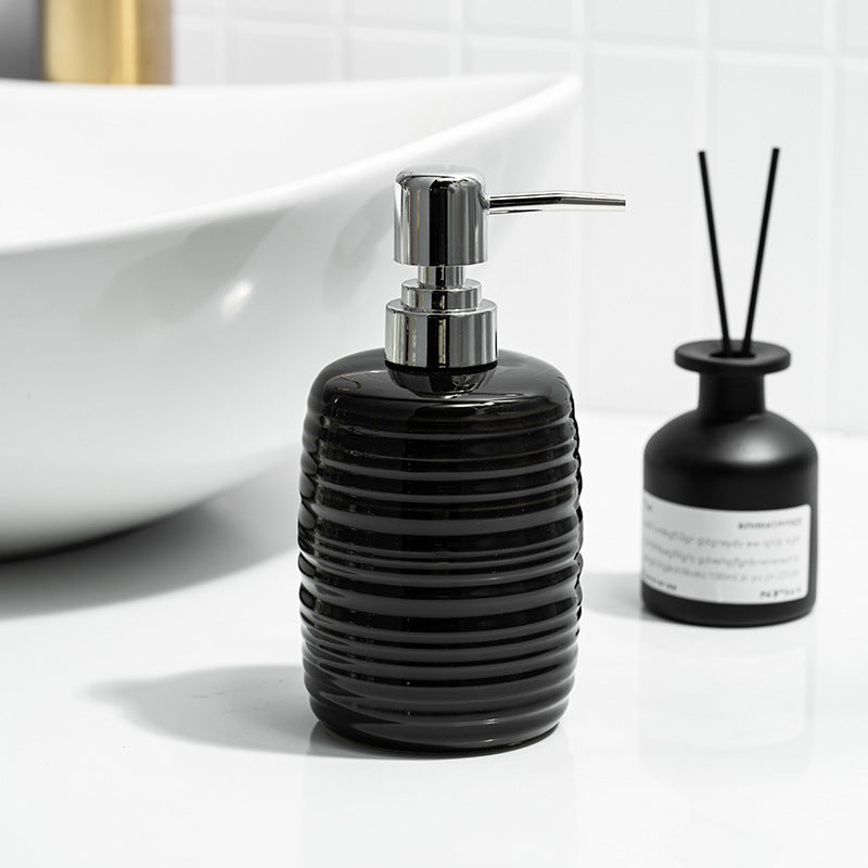 Black ribbed soap dispenser with silver pump on a white surface, next to a black diffuser bottle.