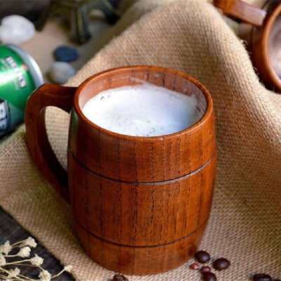 Wooden mug filled with a frothy beverage on a textured surface with coffee beans and a can.