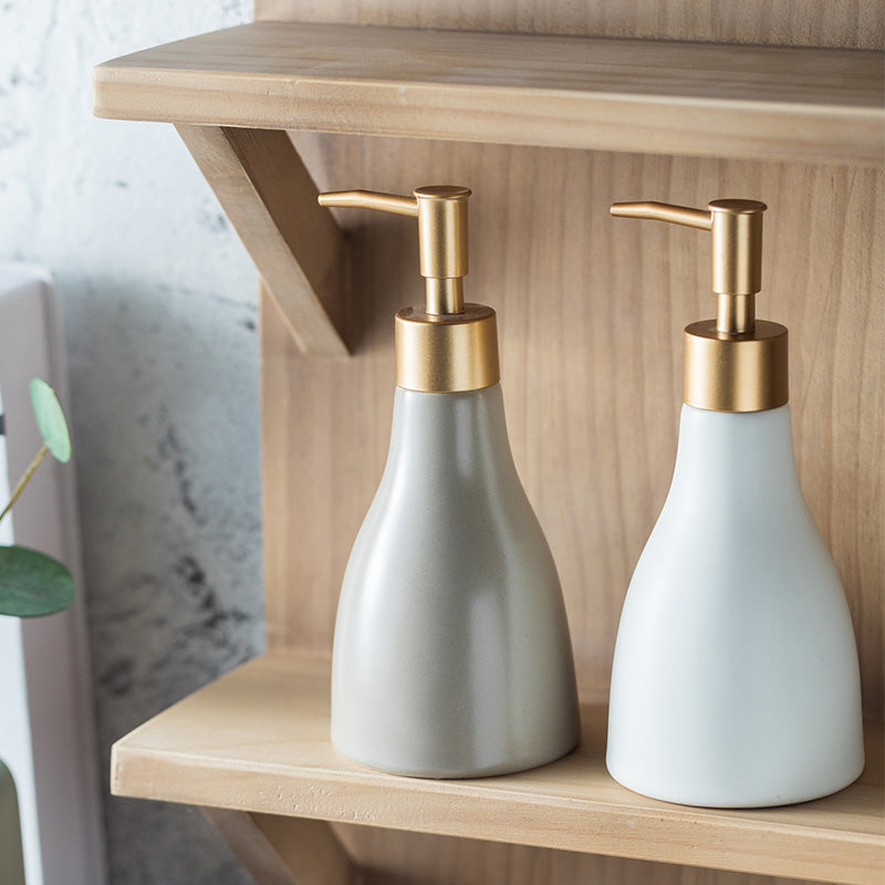 Two white soap dispensers with gold pumps on a wooden shelf.
