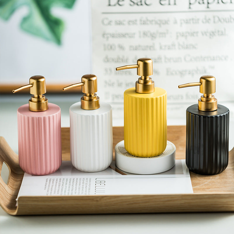 Four ceramic soap dispensers with gold pumps on a wooden tray.