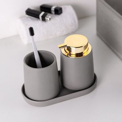 Gray toothbrush holder with gold cap and gray soap dispenser on a white surface.