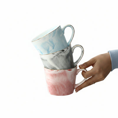 Person holding marbled ceramic mugs on a wooden tray with coffee beans and sugar cubes.
