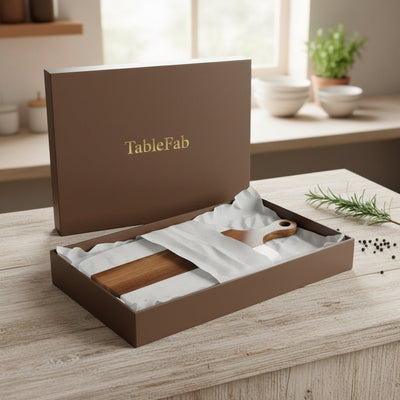 Open brown 'TableFab' box containing wooden cutlery on a wooden surface with a blurred kitchen background.