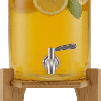 Close-up of the stainless steel spigot and wood stand on a glass beverage dispenser
