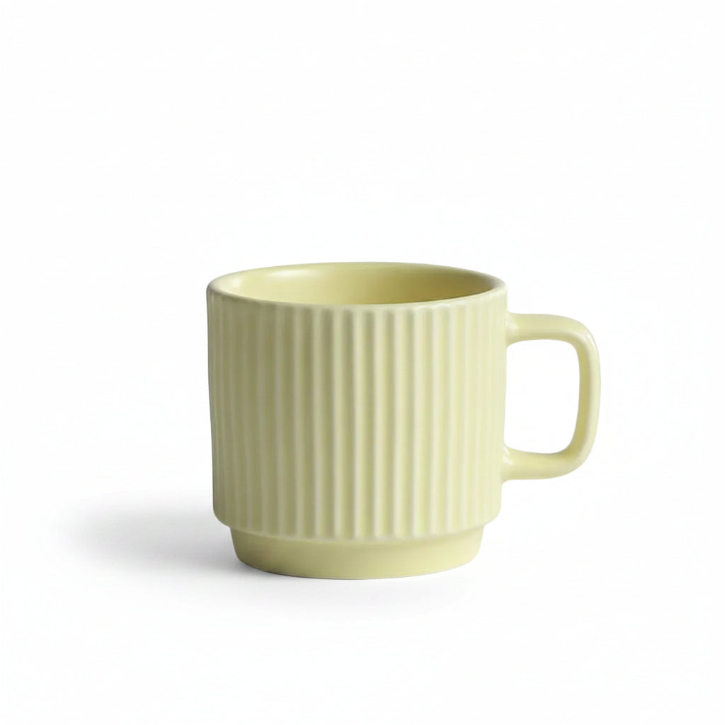 A pale yellow ceramic mug with vertical fluting and a rounded handle, set on a white textured tablecloth with a soft gray background.
