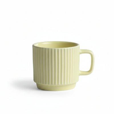 A pale yellow ceramic mug with vertical fluting and a rounded handle, set on a white textured tablecloth with a soft gray background.