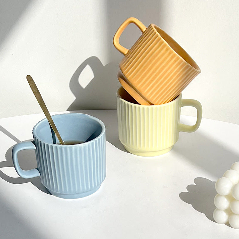 Three ceramic mugs in blue, yellow, and green on a light surface with a white background