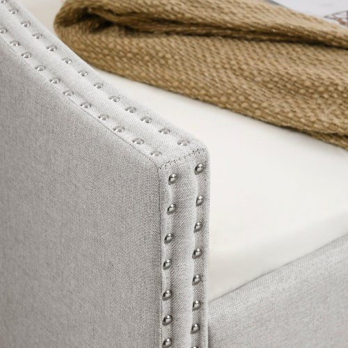 Close-up of a gray upholstered chair with studded detailing and a brown fabric item on top.