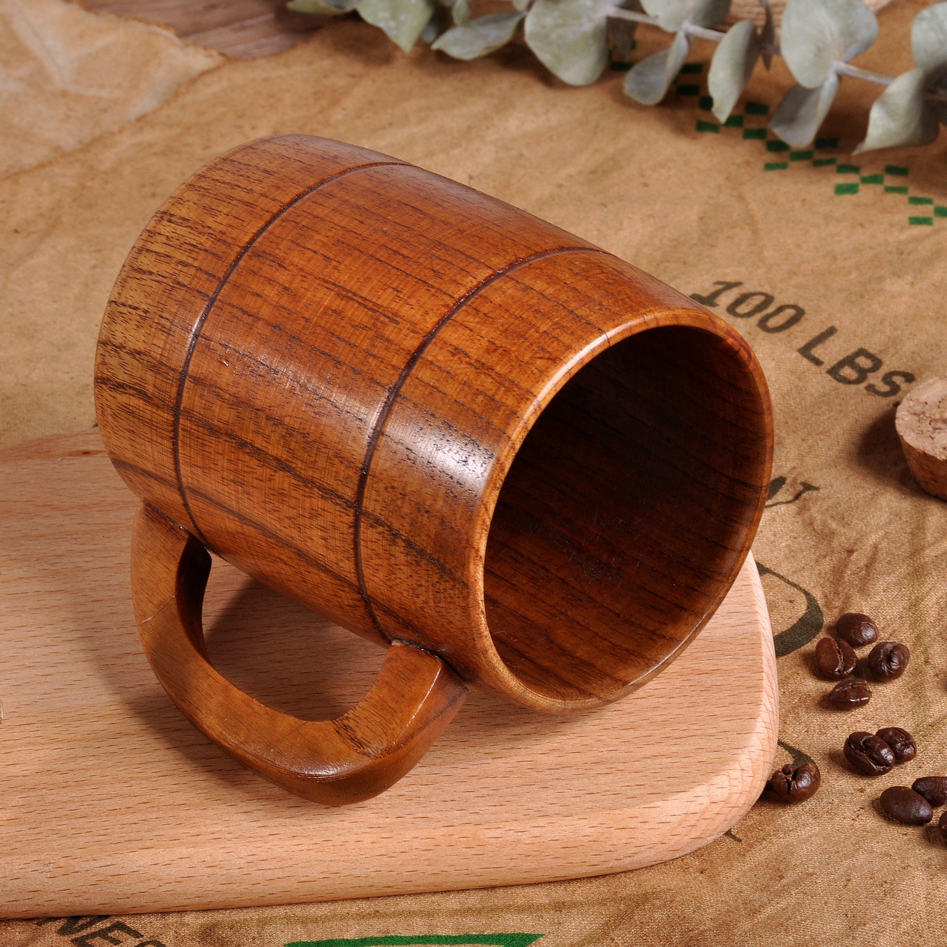 Wooden mug on a wooden surface with coffee beans and eucalyptus leaves.