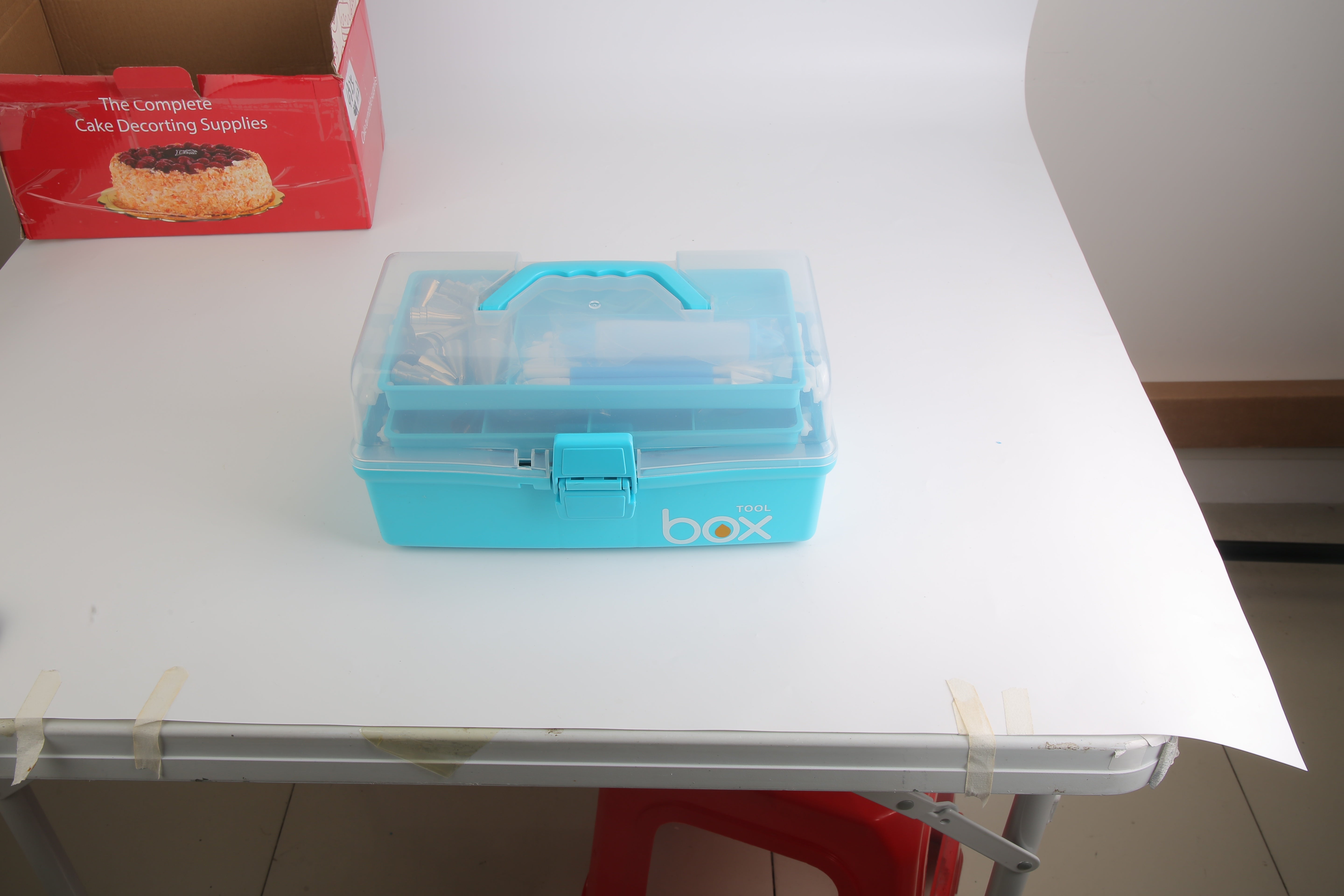 Blue toolbox on a white table with a red box in the background
