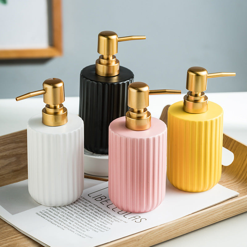 Set of four ceramic soap dispensers with gold pumps on a wooden tray.