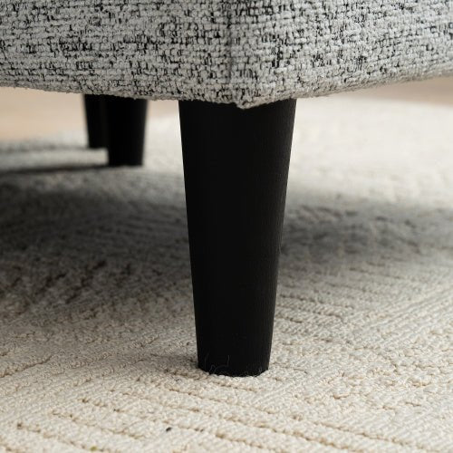 Close-up of a textured gray fabric surface with a black leg on a carpeted floor.