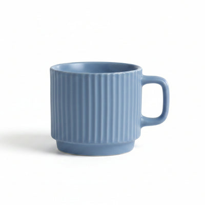 A light blue ceramic mug with vertical fluted ridges and a C-shaped handle, sitting on a white textured lace cloth with a soft gray background.