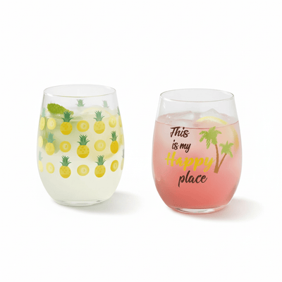 Two tropical stemless wine glasses on white background — pineapple print and palm tree Happy Place design, set of 2