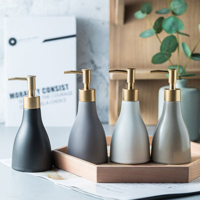 Set of four ceramic soap dispensers with gold pumps on a wooden tray.