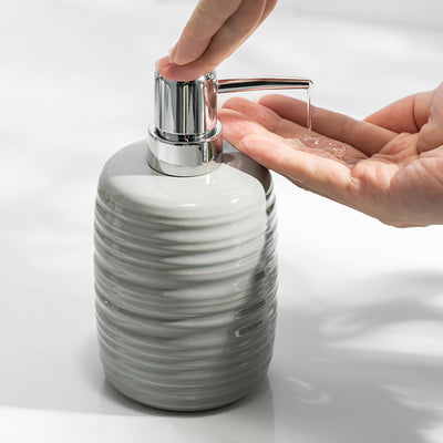 Gray marbled soap dispenser with a hand squeezing it, releasing liquid soap onto the palm.