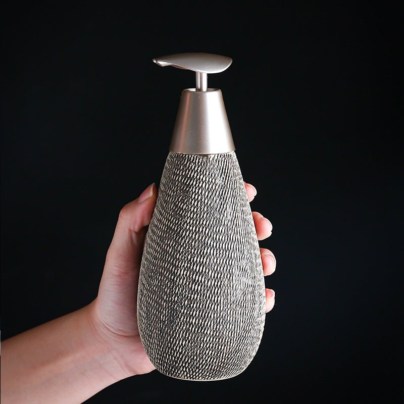 Hand holding a textured bottle with a metallic cap against a black background