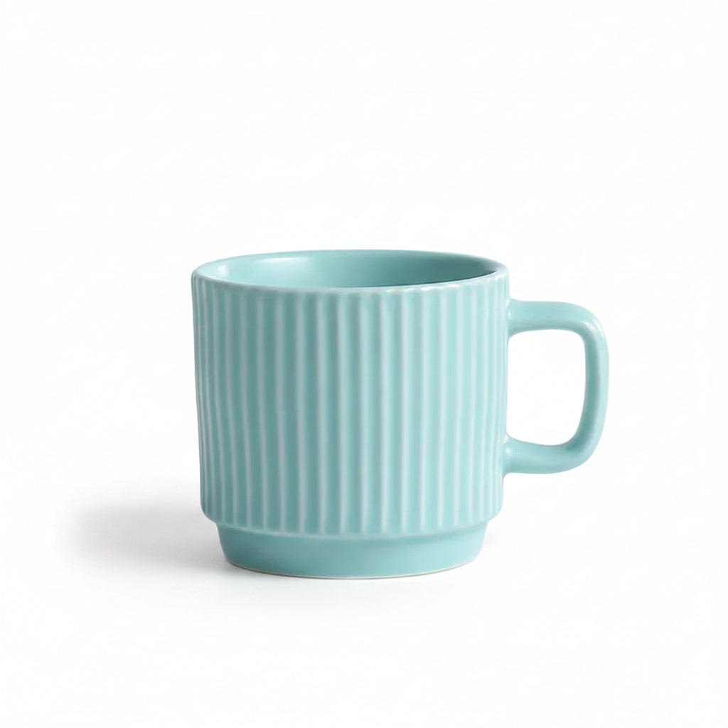 A light mint green ceramic mug with vertical fluted ridges and a matching handle, sitting on a white textured lace cloth with a decorative cream-colored candle partially visible on the left.