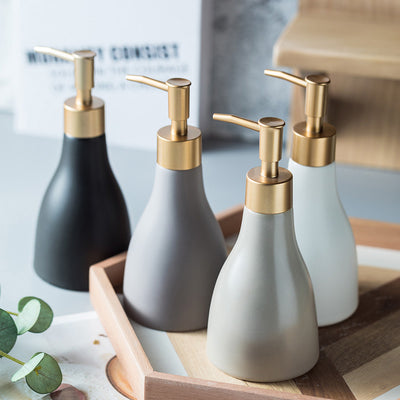 Set of four ceramic soap dispensers with gold pumps on a wooden tray.