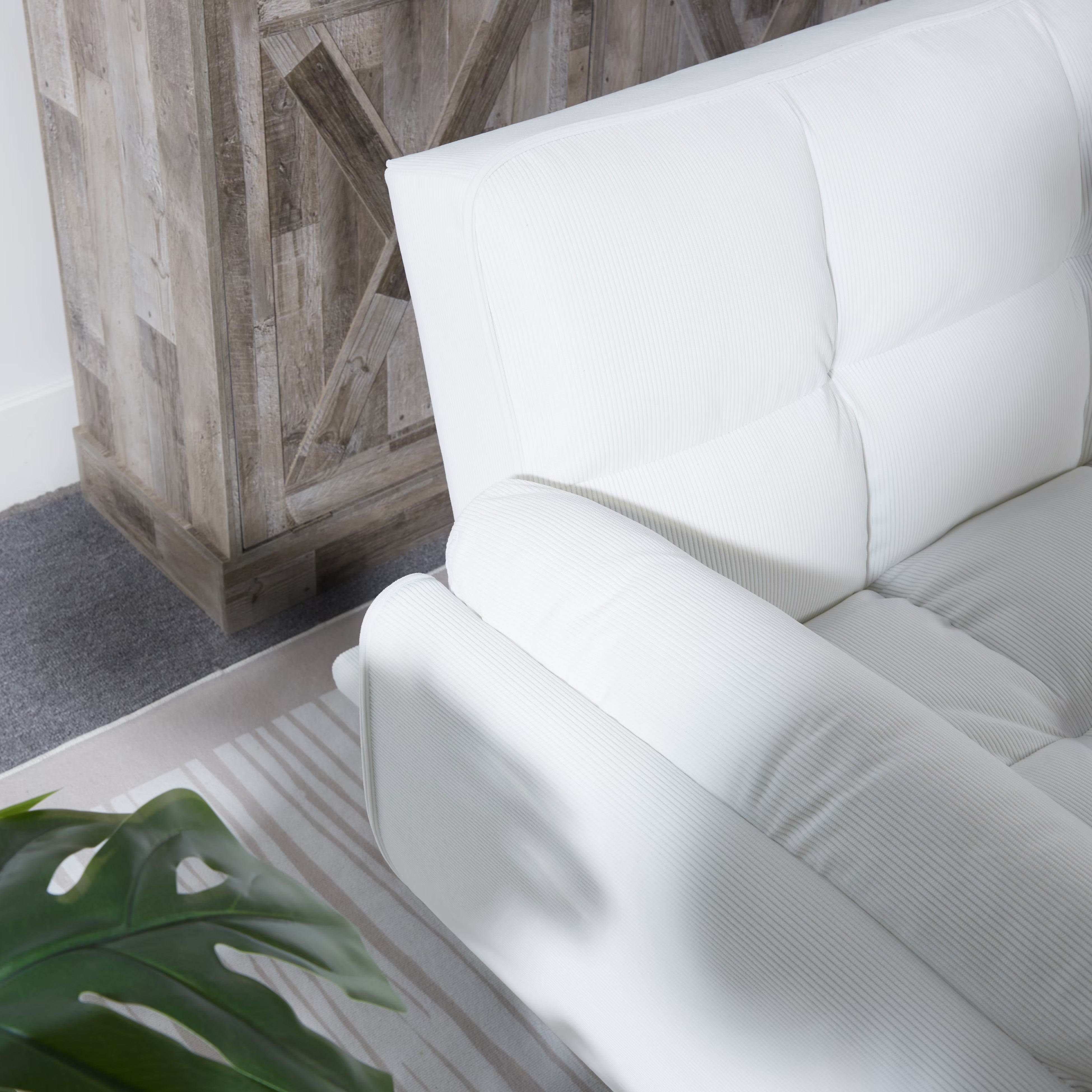 White sofa in a room with wooden wall paneling and a plant.
