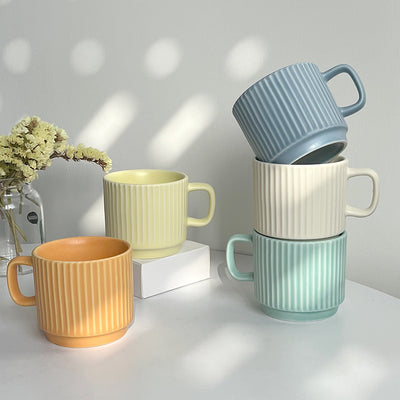 Set of colorful mugs stacked on a light surface with a minimal background