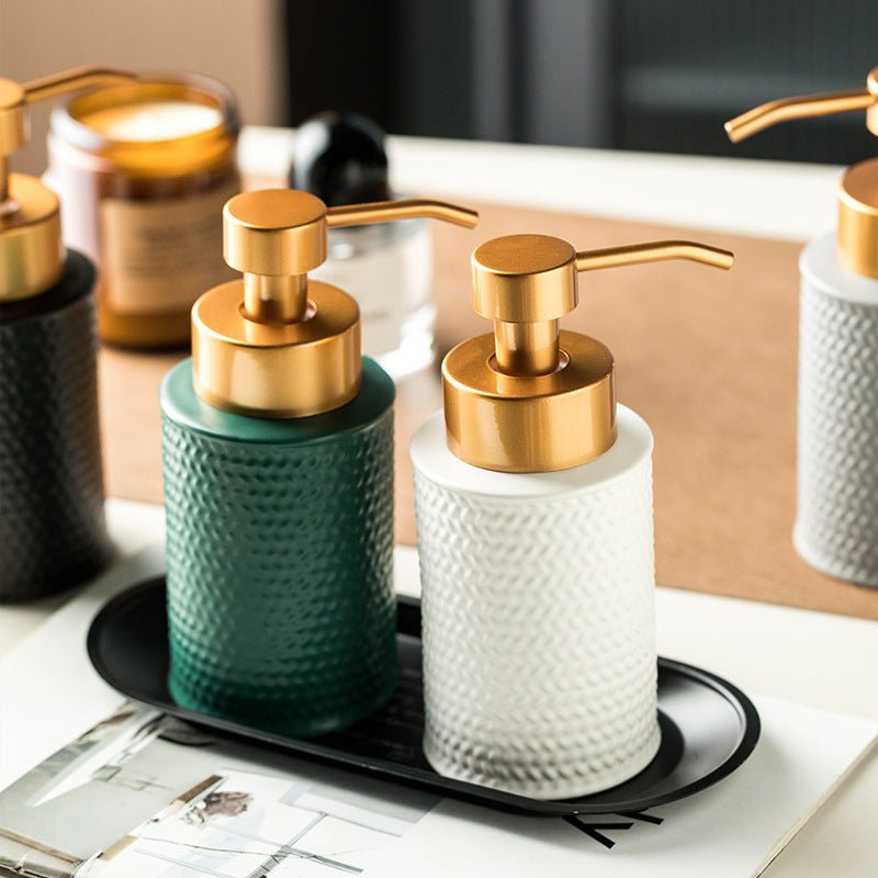 Two soap dispensers with gold pumps on a black tray in a bathroom setting.