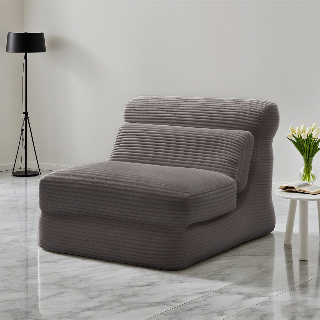 Modern gray lounge chair in a minimalistic room with a lamp and small table.