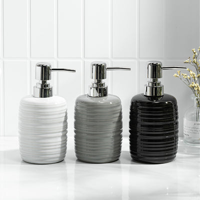 Three ceramic soap dispensers with silver pumps on a bathroom counter.