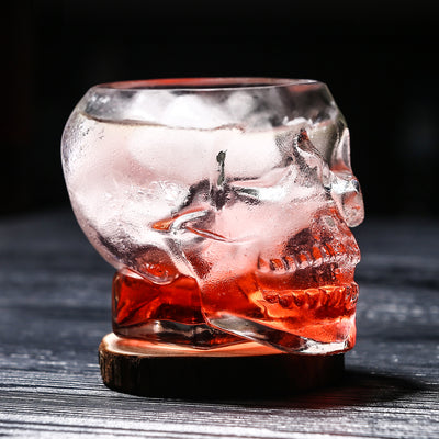 Clear glass skull-shaped drink container with red liquid on a dark surface